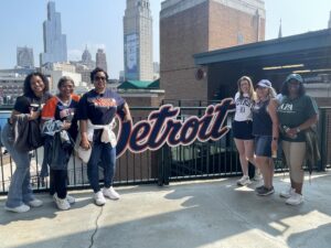 Six APA members standing in front of a sign reading "Detroit" in the Tigers font.
